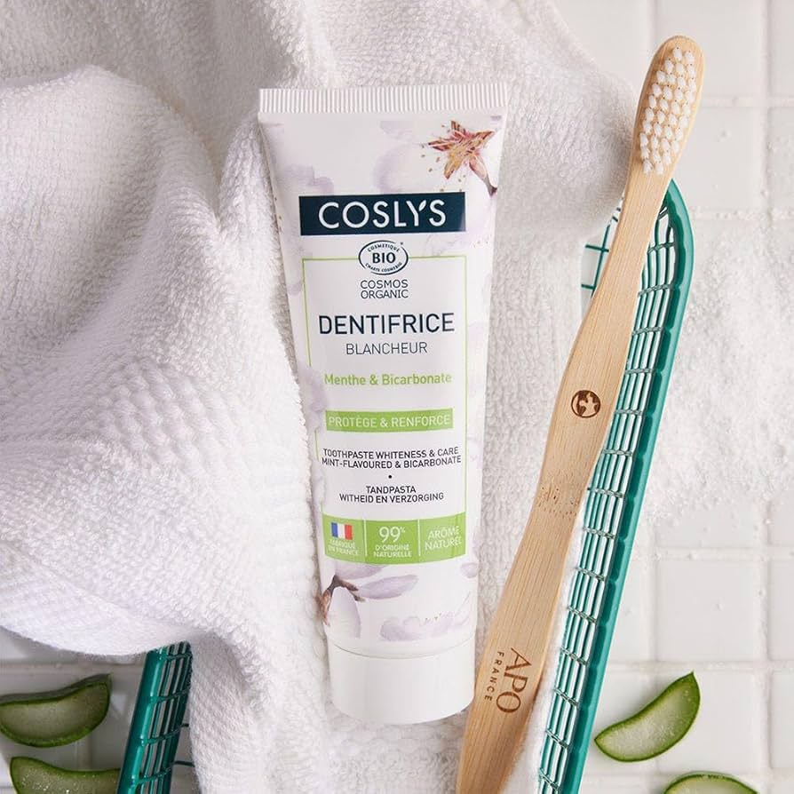 Un dentifrice blancheur bio de 75 ml de la marque Coslys posé à côté d'une brosse à dent