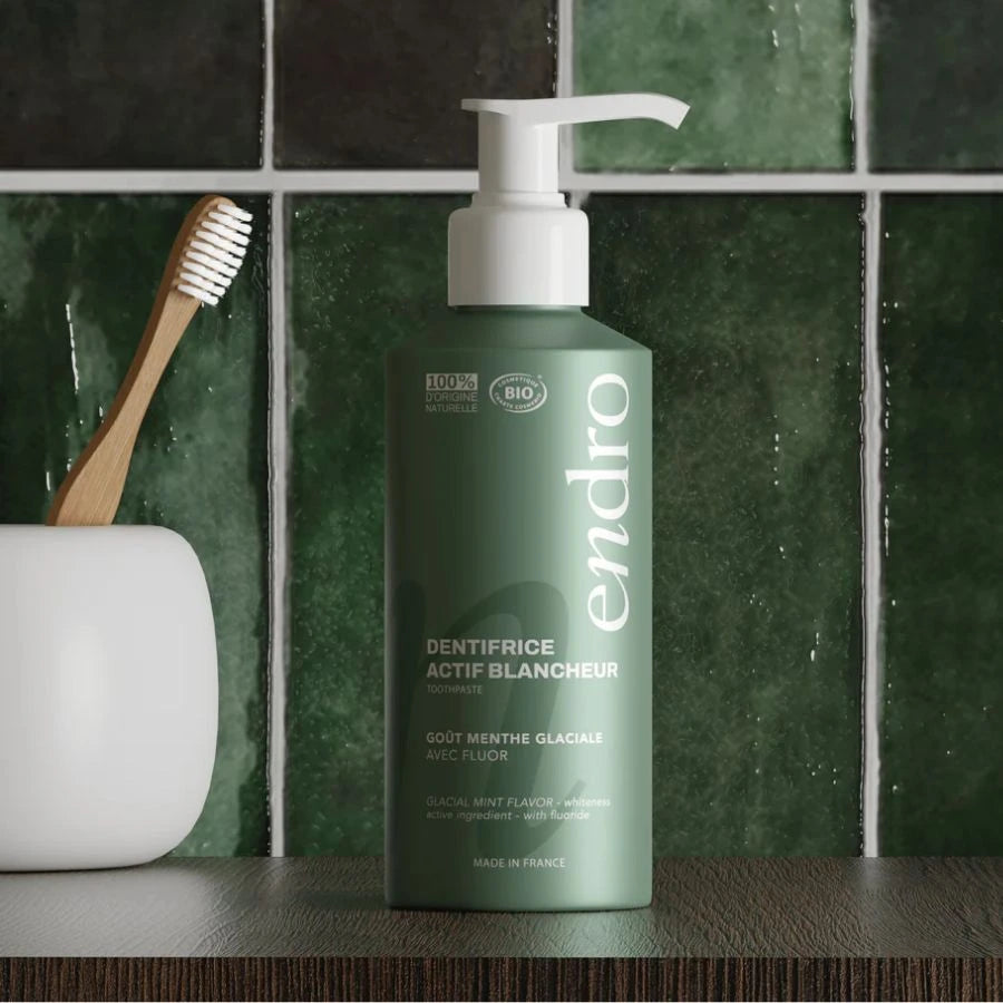 Un dentifrice actif blancheur goût menthe glaciale Endro posé à côté d'un porte brosse à dent avec une brosse à dent en bambou