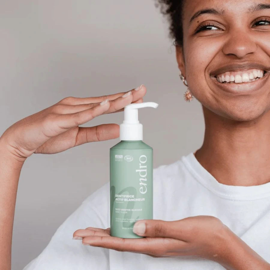 Une femme tenant un dentifrice actif blancheur goût menthe glaciale Endro