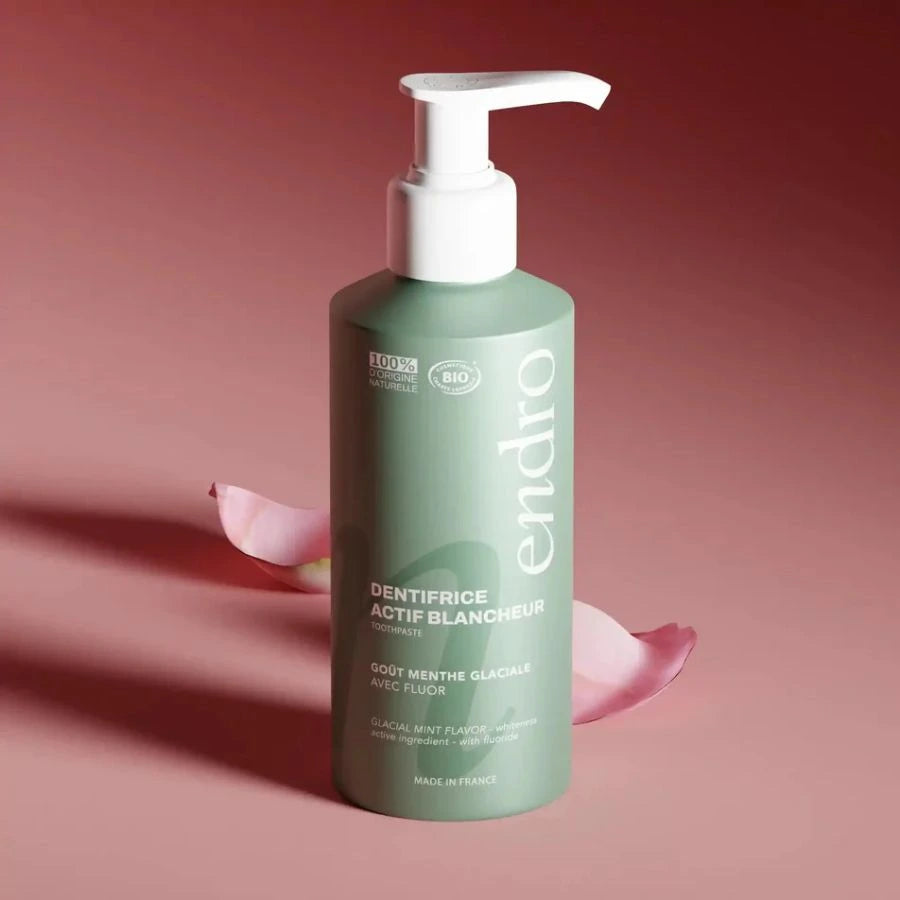 Un dentifrice actif blancheur goût menthe glaciale Endro sur un fond rose avec des pétales