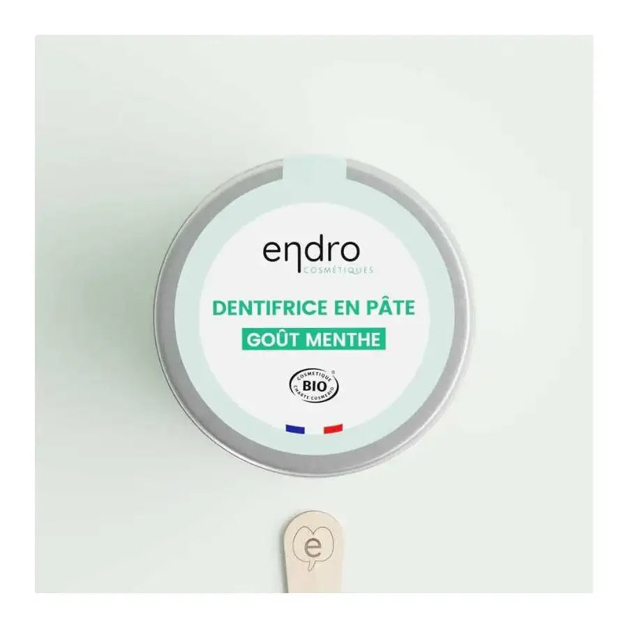 Un dentifrice en pâte goût menthe de 100 ml de la marque Endro avec un spatule en bois posé à côté