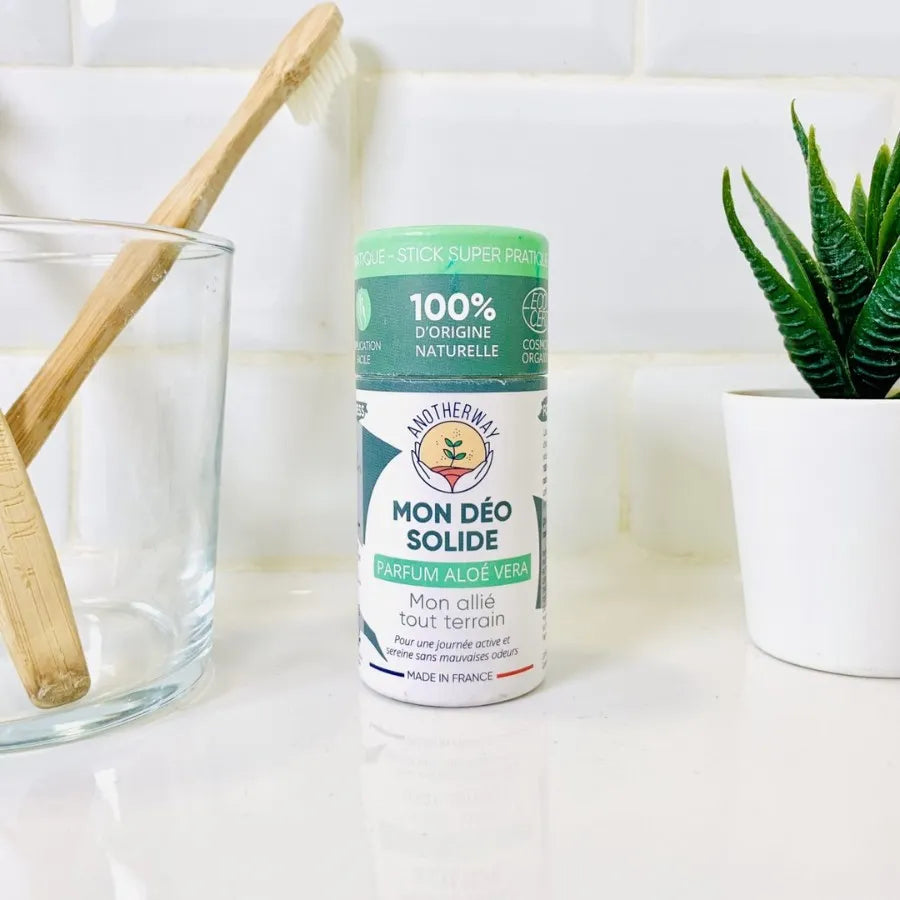 Un stick de déodorant Solide Aloé Vera Bio Anotherway posé à côté d'un verre à dent dans une salle de bain