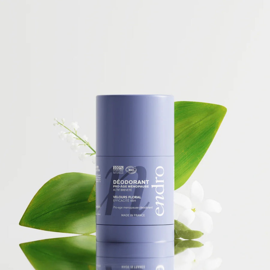 Déodorant stick Endro Pro-âge Ménopause avec feuilles vertes et fleurs blanches, pour illustrer son parfum floral et délicat.