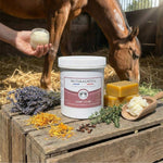 Un pot de dermi'calme de la marque naturacheval posé à côté d'ingrédients le composant avec une main tenant un pot devant un cheval