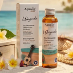 Eau Bronzante l'Originale Aquatéal en packaging luxe sur vanity côtière avec fleurs tropicales