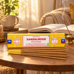 Boîte jaune et bâtonnets d'encens Satya Bois de Santal 15g, posés sur une table dans un coin lecture chaleureux avec porte-encens en laiton