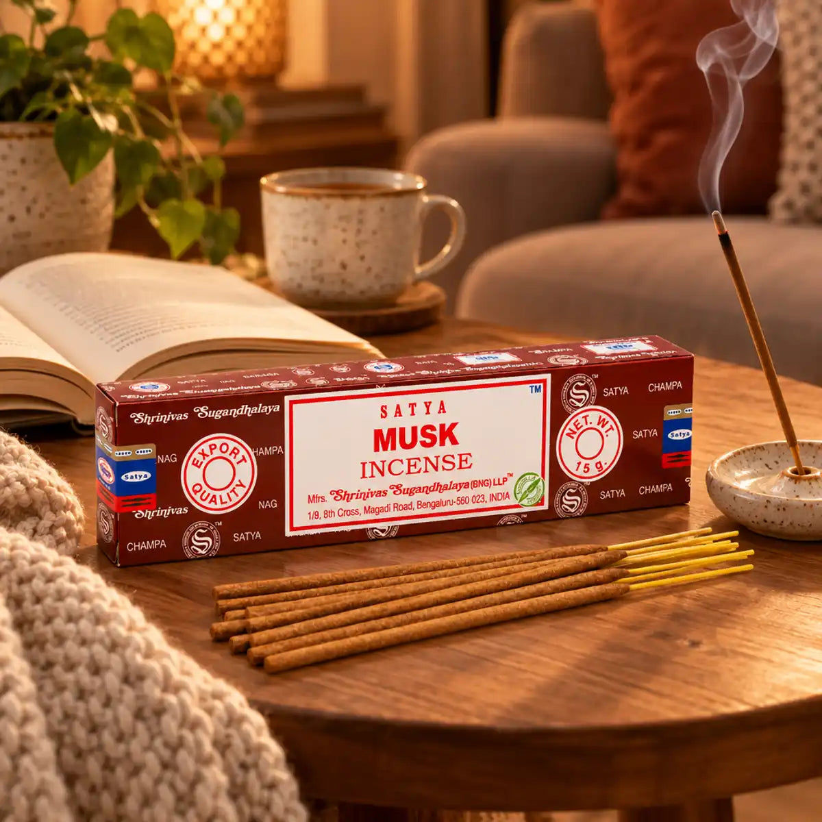 Encens Satya Musc 15g en lumière chaleureuse, bâtonnets éventails, fumée parfumée et plaid en laine sur table en bois