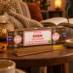 Encens Satya Oud 15g dans sa boîte marron, posé sur une table en noyer avec bâtonnets et fumée douce, ambiance chaleureuse