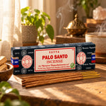 Encens Satya Palo Santo 15g en boîte bleu marine, posé sur une étagère en bois avec bâtonnets non allumés et fumée parfumée