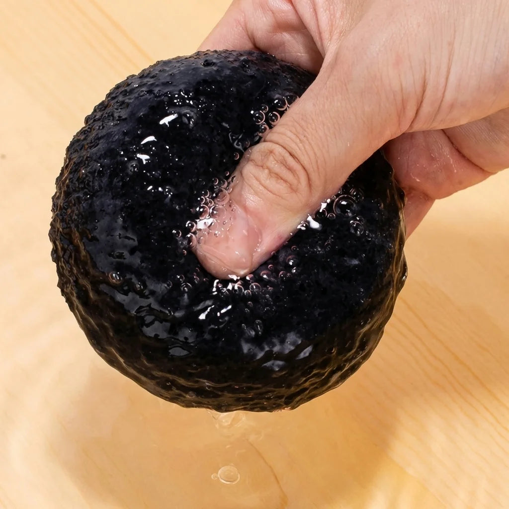 Éponge Konjac Bio Kyuké au Charbon actif noire texturée dans une main sur fond bois