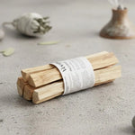 Un fagot de bâtons de palo santo de la maque Veegreen, sur une table en marbre beige, avec une sauge en arrière plan