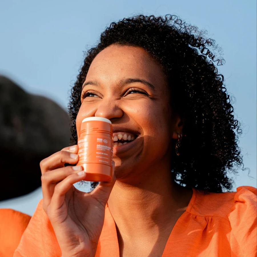 Femme souriante tenant un déodorant stick Endro Éclat Soleil en extérieur, pour illustrer l’utilisation du produit au quotidien.