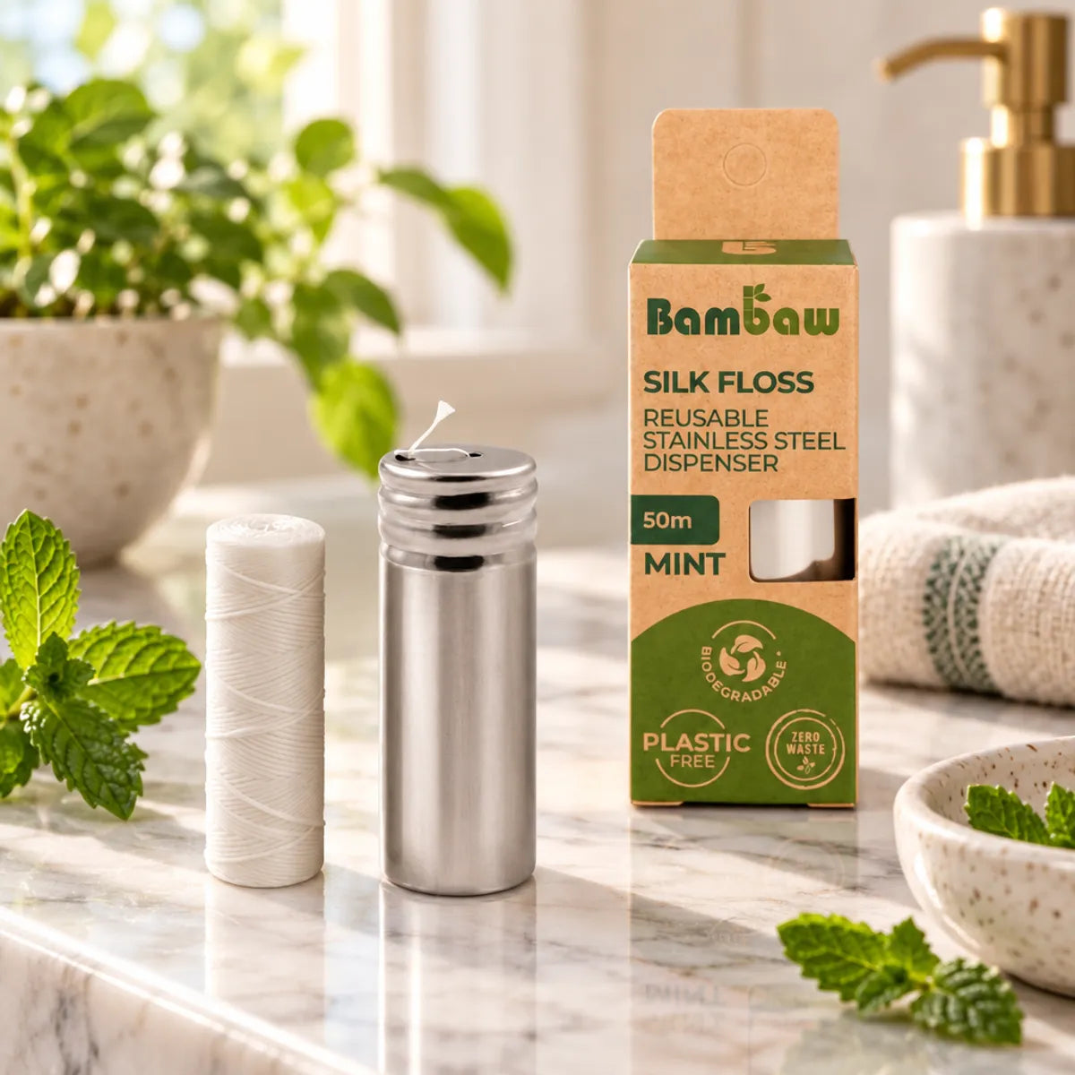 Fil dentaire en soie Bambaw avec distributeur inox et recharge de 50m, posé sur un plan de toilette en marbre