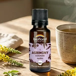 Flacon compte-gouttes Fleur de Bach Aigremoine Biofloral sur table en bois, avec tisane et brins d'aigremoine jaune