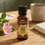 Flacon ambré Fleur de Bach Wild Rose (Eglantier) Bio en granules, sur table en bois avec roses sauvages et tasse de thé