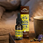 Flacon compte-gouttes SOS Nuit Fleurs de Bach Biofloral 20 ml sur une table de chevet en bois, à côté d'une tasse de tisane et de fleurs sauvages bleues