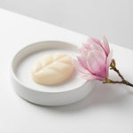 Fondant de cire Magnolia Scentships dans un plat blanc avec branche de fleur rose sur fond minimaliste