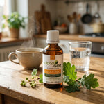 Flacon compte-gouttes ambré Gem-Tonic 16 Bio Alphagem 50 ml sur une table en bois, avec tisane, eau et bourgeons de cassis