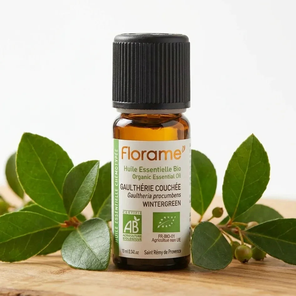 Flacon d'huile essentielle Gaulthérie couchée Bio Florame 10ml avec feuilles fraîches sur bois naturel