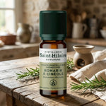 Flacon ambré de 10 ml d'huile essentielle de romarin à cinéole bio Saint-Hilaire, posé sur une table en chêne avec brins de romarin frais
