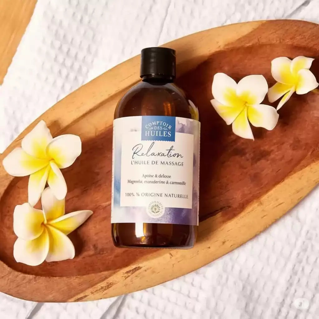 Une huile de massage relaxation de la marque comptoir des huiles en 250 ml  posée sur une coupelle en bois avec des fleurs de frangipanier