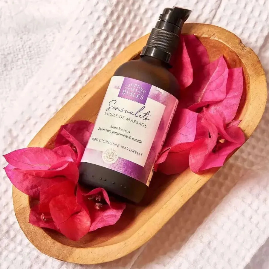 Une huile de massage sensualité de la marque comptoir des huiles en 100 ml  posée sur des fleurs dans un récipient en bois