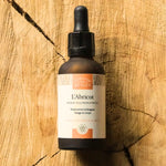 Un flacon de 30 ml d'Huile d'Abricot Bio 30ml Visage & Corps - Comptoir des Huiles, posé sur une planche en bois rustique