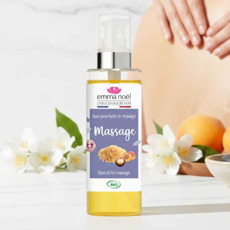 L'huile de massage Emma Noel. Des fleurs blanches sont plaçés à l'arrière du produit.