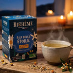 Boîte d'infusion bio Biohême « À la belle étoile » bleu marine sur table en bois, tasse fumante, fleurs de camomille, soir étoilé