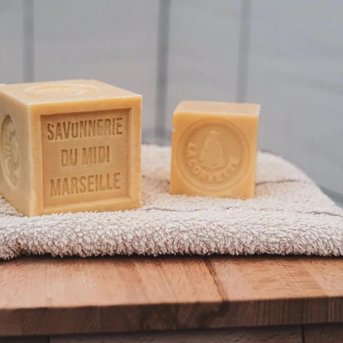 Cube Savon de Marseille 500g La Corvette 72% huiles végétales posé une serviette de toilette.