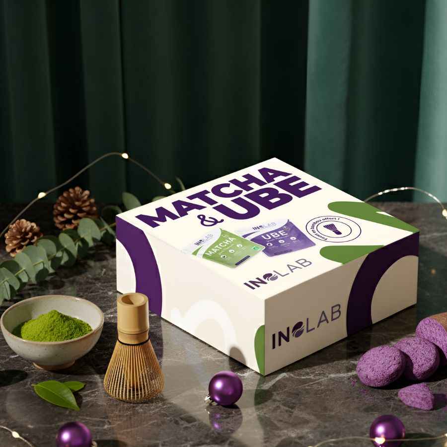 Un coffret de match et d'ube avec un fouet, un bol de poudre de matcha et de l'ube avec des boules de noël, des pommes de pins et de l'eucalyptus