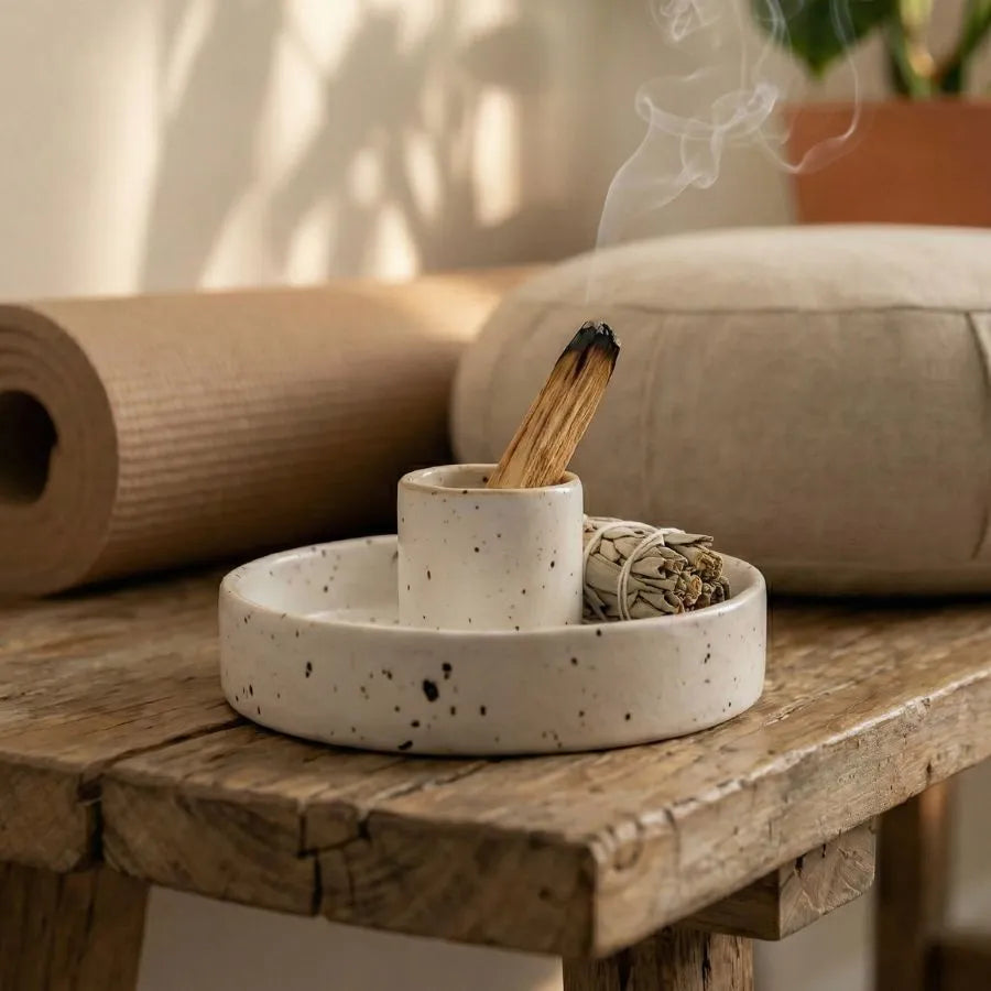 un porte palo santo moucheté posé sur un banc en bois avec une sauge et un palo santo fumant