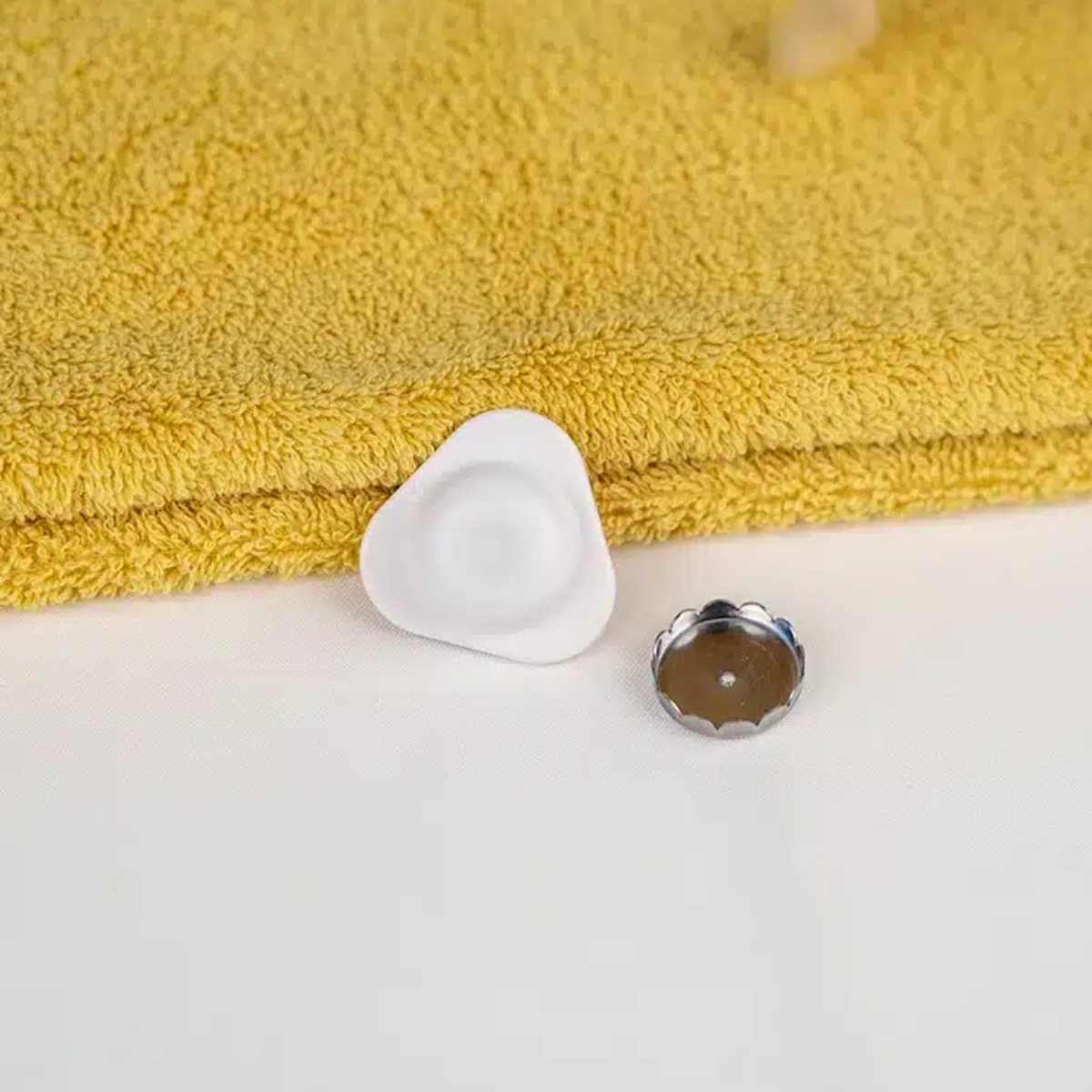 Porte savon triangle blanc adhésif de la marque Apimani  posé sur une serviette
