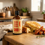 Bouteille de sauce piquante bio Frenchie X ambrée à côté d'un croque-monsieur doré, de carottes et patates douces rôties (Chiki Bam)