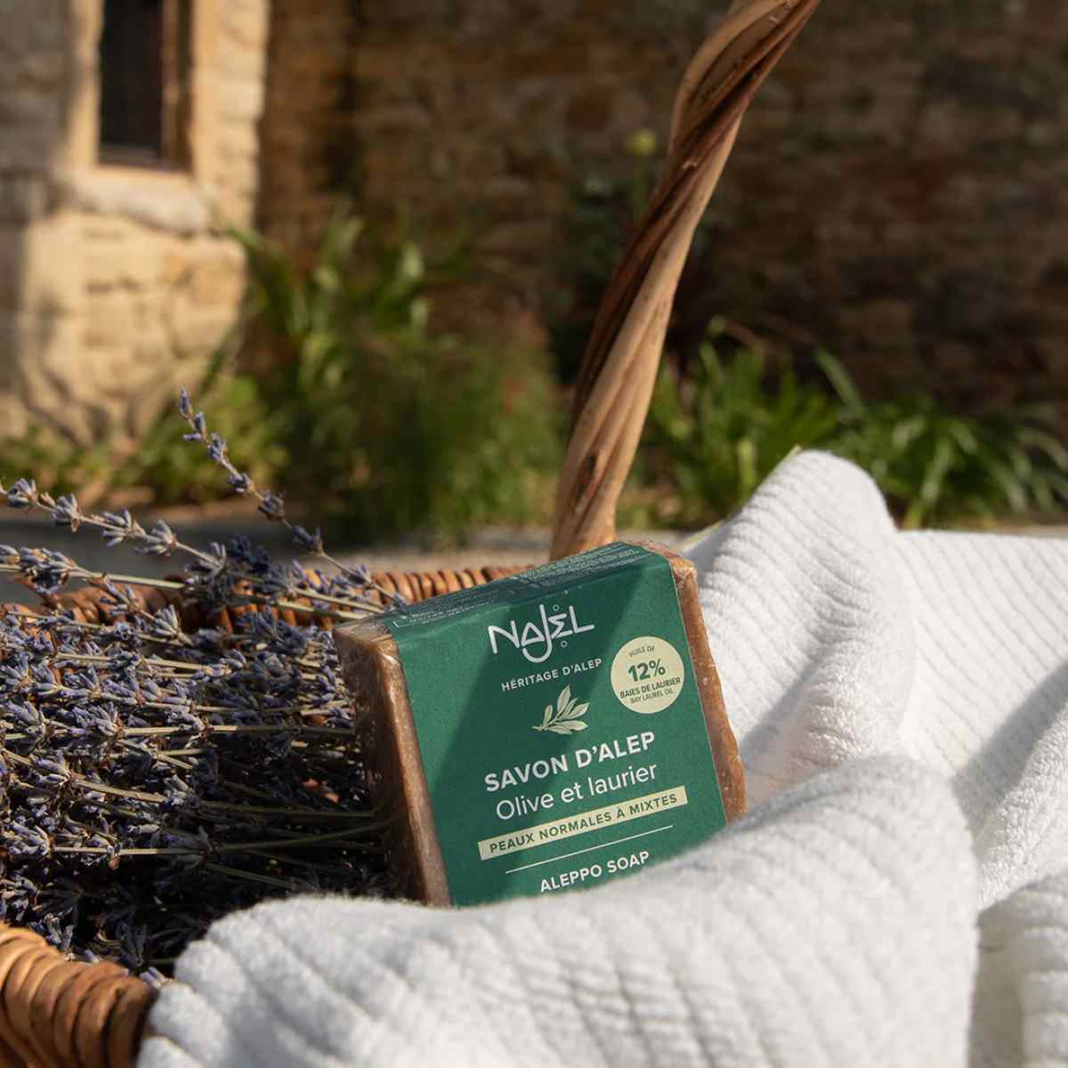 Savon d'alep olive et laurier 12% Najel posé sur un panier en osie, un linge blanc et de la lavande