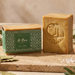 Savon d'Alep Al Bara 200g laurier avec emballage vert et feuilles séchées sur fond neutre