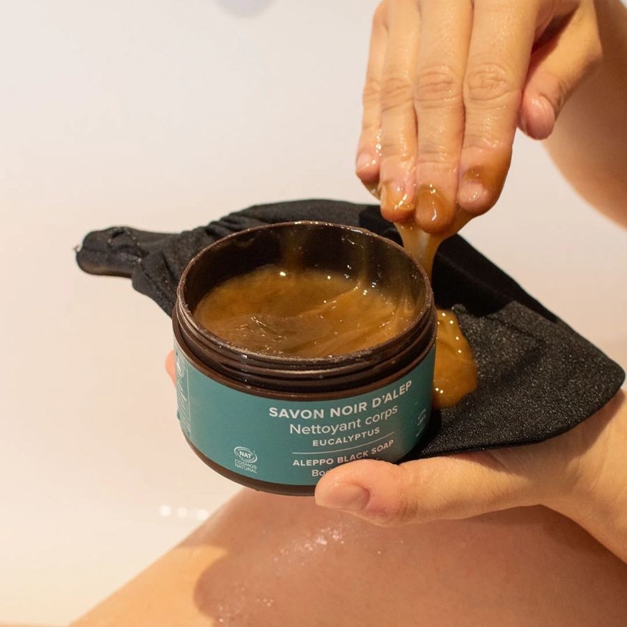 Main prélevant du savon noir d’Alep à l’eucalyptus 180 g Najel dans son pot