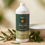 Savon noir liquide Najel bio 1L avec branches d'olivier et feuilles de laurier sur bois naturel