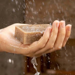 Une main tenant un savon exfoliant aux tourteaux de moringa sous la douche