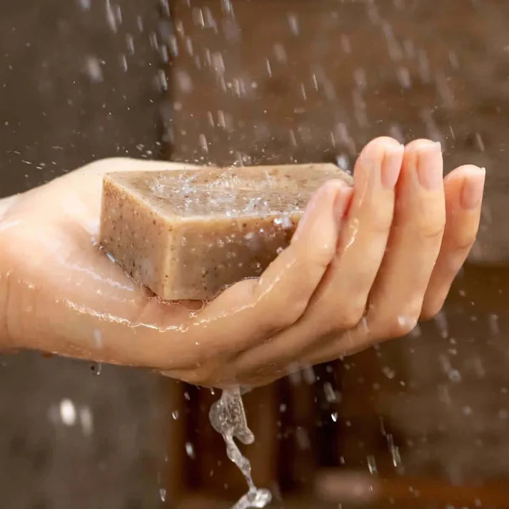 Une main tenant un savon exfoliant aux tourteaux de moringa sous la douche