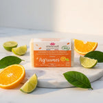 Savonnette Agrumes Bio Emma Noël 100g sur marbre blanc avec agrumes frais et feuilles vertes
