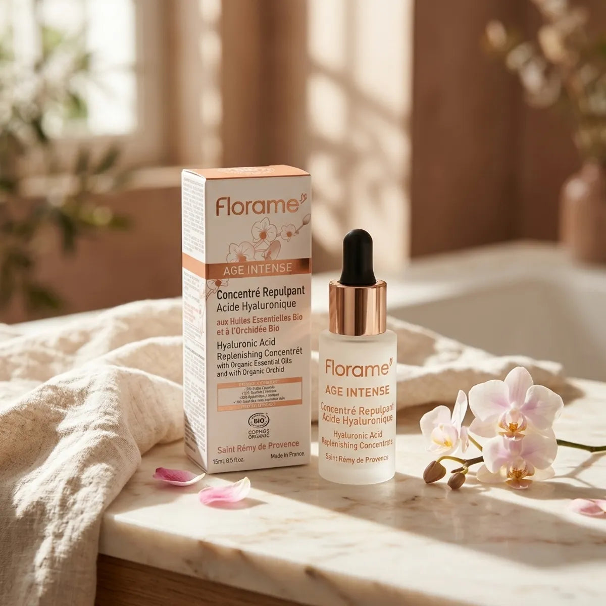 Flacon en verre dépoli du sérum Florame Âge Intense à l'acide hyaluronique bio, posé sur un comptoir en marbre près de sa boîte