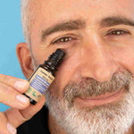 Un homme tient le serum contour des yeux et l'applique sur ses cernes et poches