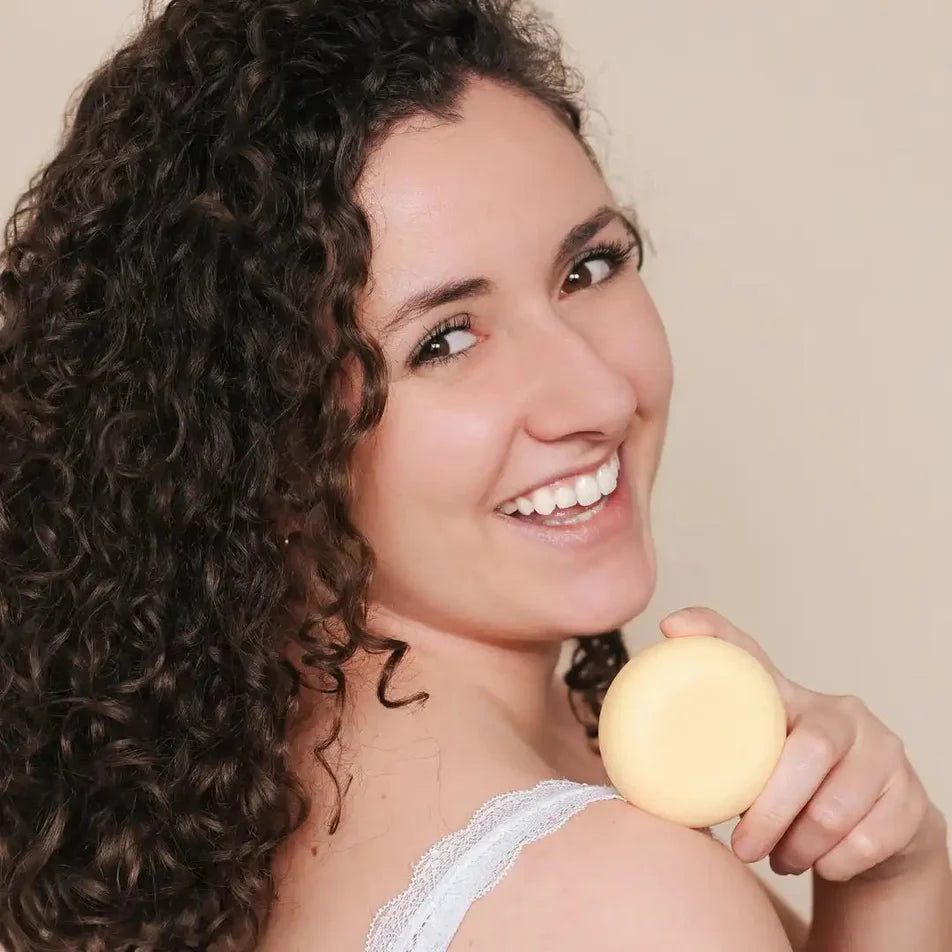 Une femme aux cheveux bouclés tenant un shampoing solide pour cheveux bouclés de la marque Endro