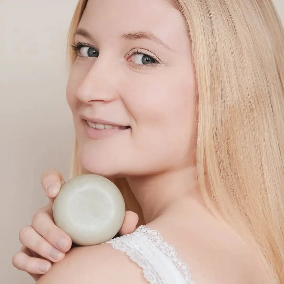 Une femme blonde tenant un shampoing pour cheveux gras de la marque Endro