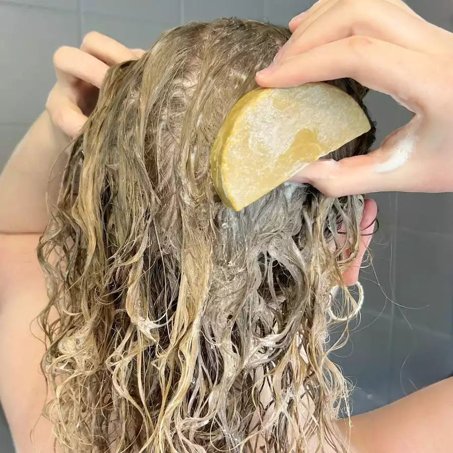 Une femme en train de se laver les cheveux avec un shampoing solide à l'huile d'argan pour cheveux secs de la marque comme avant