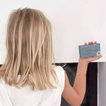 Une petite fille aux cheveux blonds de dos tenant un shampoing solide au pigment bleu ultramarine pour cheveux blonds et blancs de la marque comme avant
