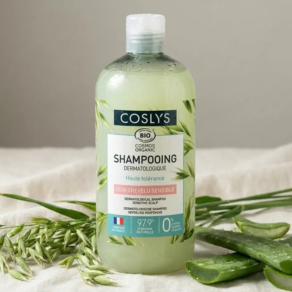 Shampooing dermatologique bio Coslys 500ml entouré de feuilles d'aloe vera et tiges d'avoine sur fond naturel