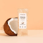 La recharge de shampoing nourissant à diluer parfum coco, posé devant une noix de coco ouverte