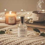 Un spray d'ambiance jasmin de madagascar de la marque Drake posé sur un plaid en laine avec des bougies et une tasse de thé